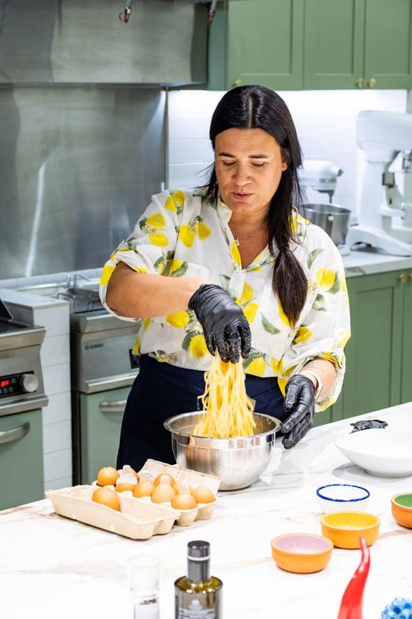Giordana lifting fresh pasta into the bowl, a tray of eggs at her elbow