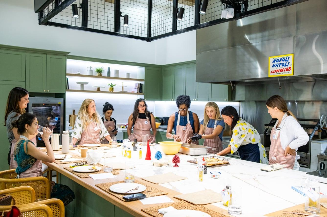 A cooking class at work around the marble island, the Napoli Napoli sign over the pass