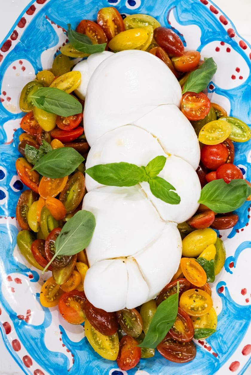 Burrata over heirloom tomatoes on a hand-painted platter, at Jou Jou Brasserie