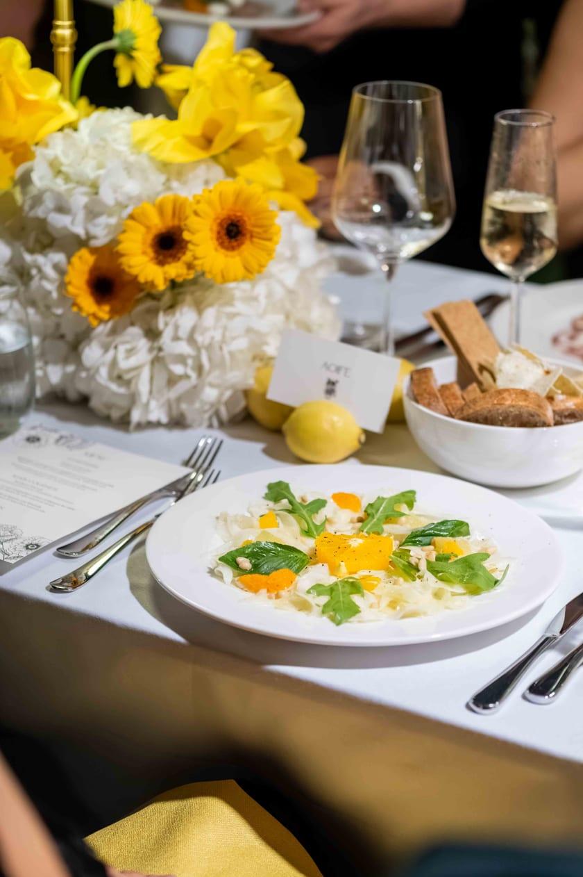 The table laid with yellow flowers, a first course and a glass of wine