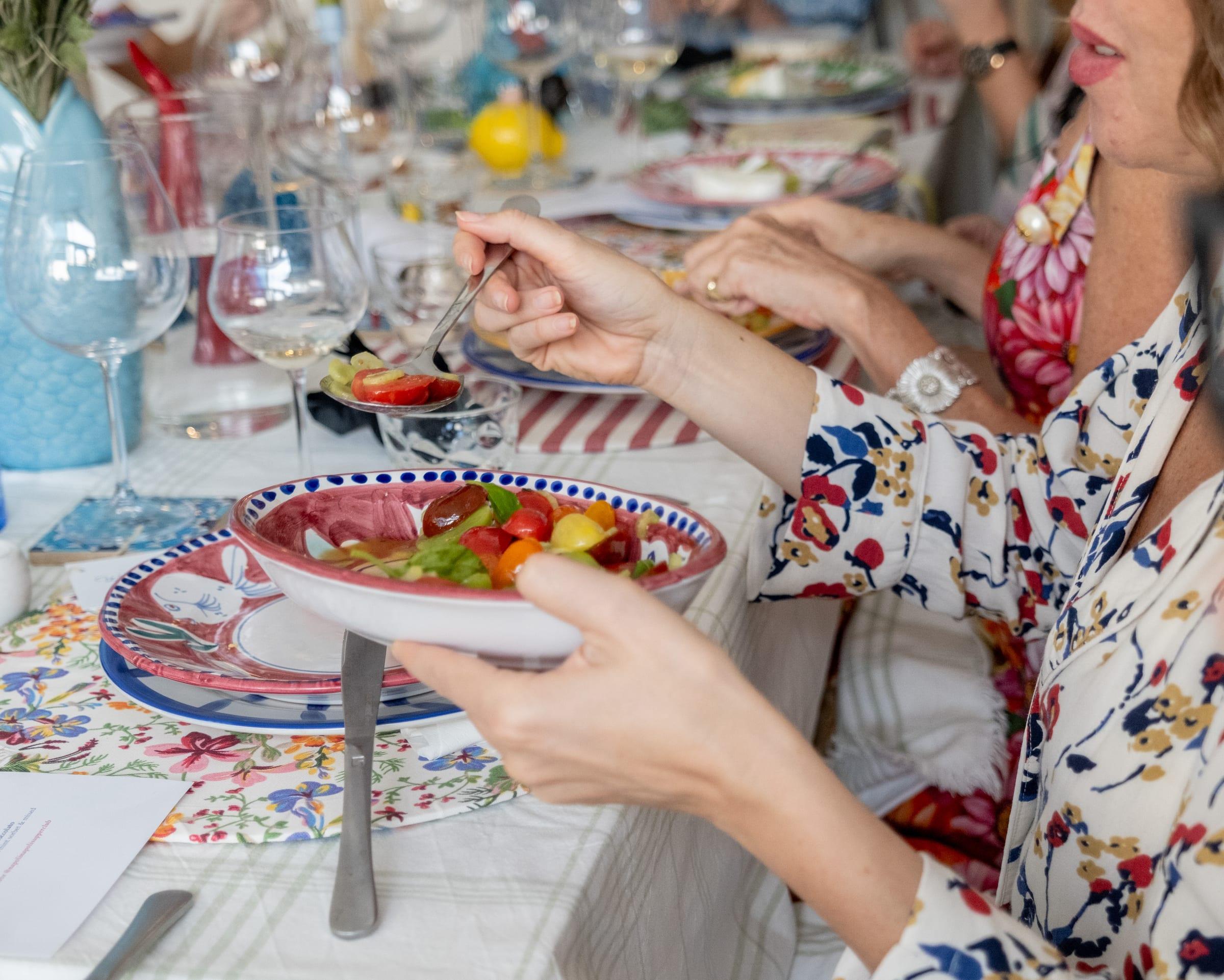 A guest serving herself tomato salad from a hand-painted bowl at a long laid table