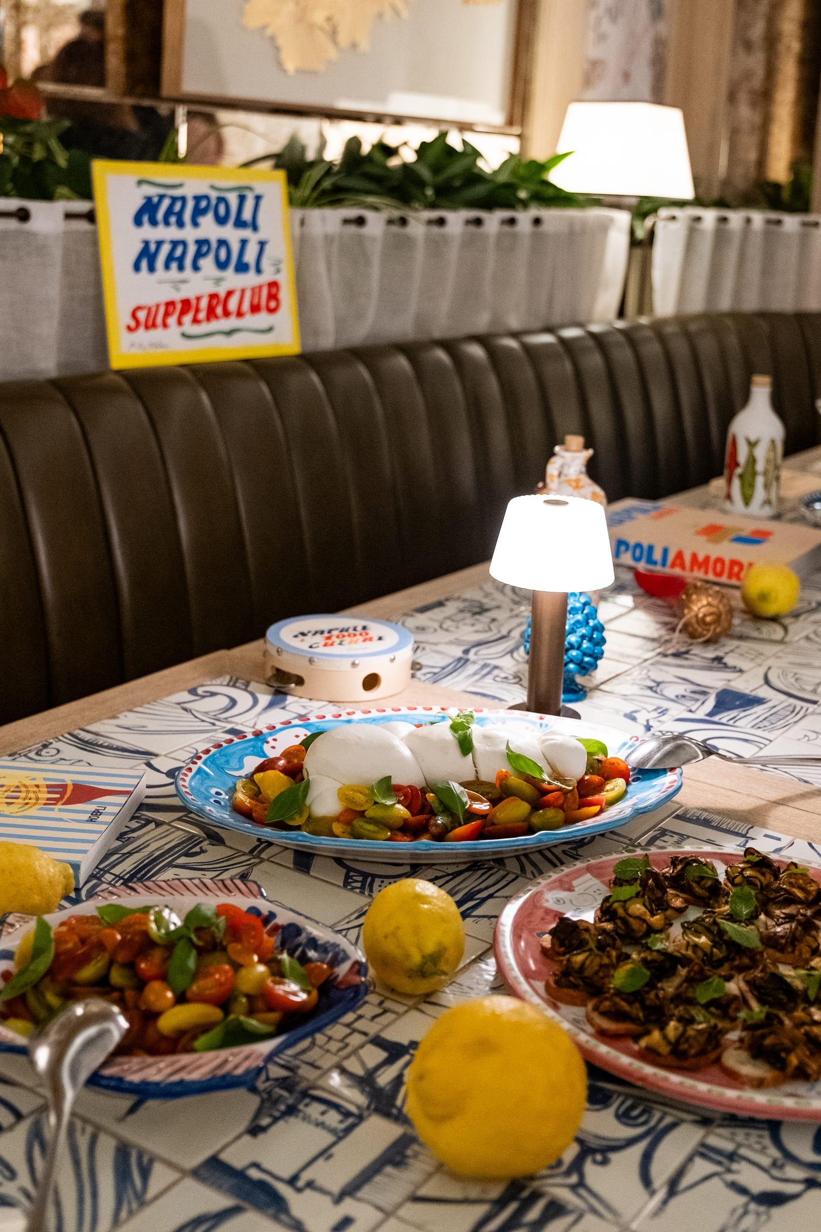 A Napoli Napoli table laid in a restaurant: the hand-painted sign, a branded tambourine and a platter of burrata
